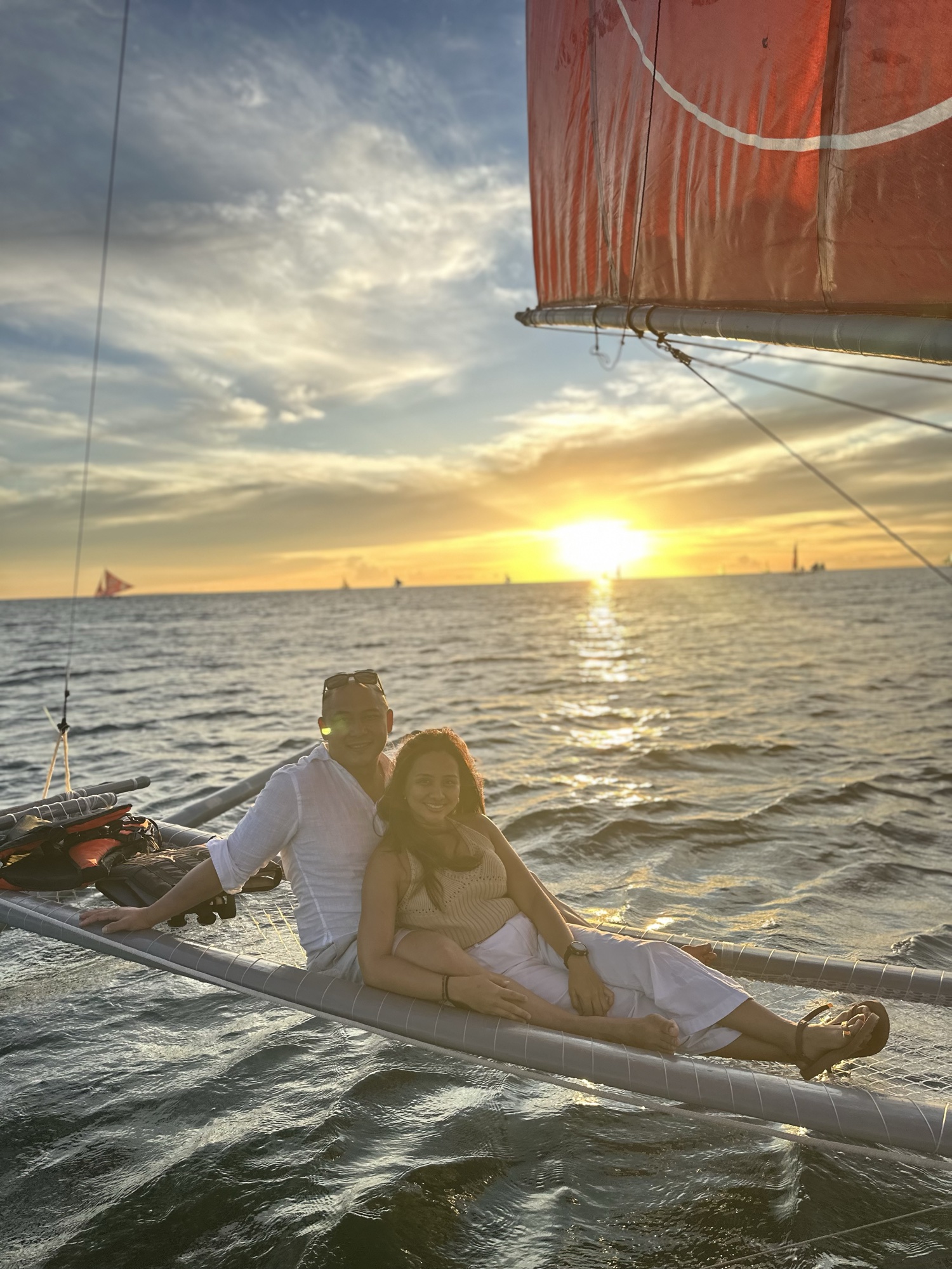 David and Chai sitting together on the outrigger of the sailboat at sunset.